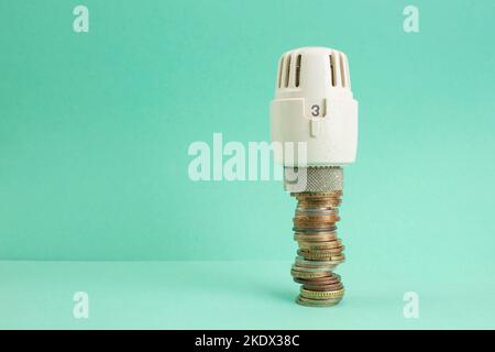 Heizthermostat Knopf auf einem Stapel von Münzen auf grünem Hintergrund. Heizpreise Konzept. Stockfoto