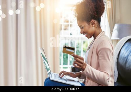 Einkaufen vom Sofa aus. Eine attraktive junge Frau, die online einkaufen und sich zu Hause auf dem Sofa entspannen kann. Stockfoto