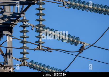 Isolatoren, die in Hochspannungsfreileitungen verwendet werden, stehen tagsüber unter blauem Himmel Stockfoto