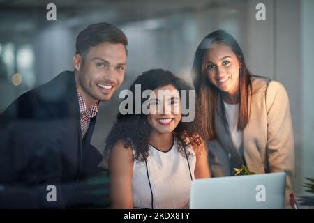 Drei Köpfe sind besser als einer. Porträt von drei Kollegen, die im Büro an einem Laptop arbeiten. Stockfoto