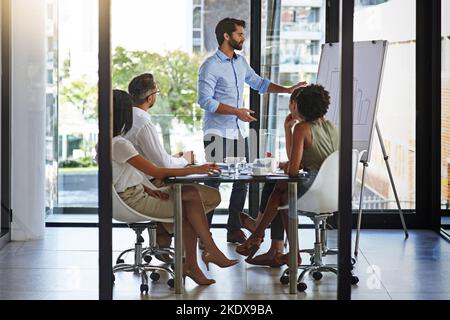 Erläuterung der Ergebnisse des letzten Quartals mit dem Team. Eine Gruppe von Männern, die Kollegen in einem Sitzungssaal eine Whiteboard-Präsentation halten. Stockfoto