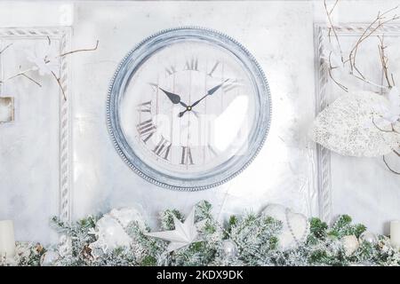 Runde hölzerne Uhr auf weißer Wand, Feier, Heimtextilien, magische Winterzeit. Verzierte Christbaumzweige und Wand mit großer Uhr Stockfoto