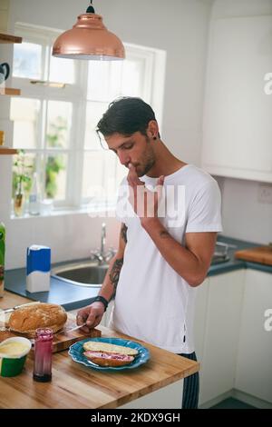 Das ist ein leckeres Sandwich. Ein hübscher junger Mann steht in seiner Küche und macht ein Sandwich. Stockfoto