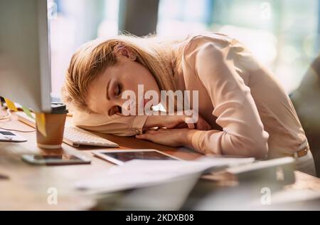 Das ist ein langer Tag... eine erschöpfte junge Geschäftsfrau, die an ihrem Schreibtisch in einem Büro schläft. Stockfoto