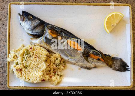 Larnaca, Zypern. 24.. Mai 2022. Ein traditionelles zyprioisches Gericht mit Fisch aus dem ganzen Seebarsch, der mit Reis gegrillt wird.die Republik Zypern steht an einem historischen und kulturellen Scheideweg zwischen Europa und Asien. Seine Hauptstädte - die Hauptstadt von Nikosia, Limassol, Famagusta und Paphos haben die Einflüsse von Generationen von Eroberern, Pilgern und Reisenden absorbiert und haben eine Atmosphäre, die sowohl kosmopolitisch als auch provinziell ist. Heute ist Zypern ein beliebtes Touristenziel für Besucher aus Europa, das von Hochzeitsreisenden bevorzugt wird (Foto: © Ruaridh Stewart/ZUMA Press Wire) Stockfoto