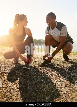 Sind Sie bereit? Ein fraues junges Paar, das ihre Schnürsenkel vor einem Lauf im Freien bindet. Stockfoto