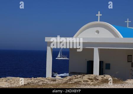 26. Mai 2022, Larnaca, Zypern: Das Segelboot fährt hinter der Agioi Anargyroi-Kirche am Kap Greco vorbei und liegt am Rand einer vertikalen Felsklippe über dem Meer. Es ist den Heiligen Kosmas und Damianos gewidmet. Unterhalb der Kapelle befindet sich eine Höhle mit dem heiligen Wasser der Heiligen. Die Republik Zypern steht an einem historischen und kulturellen Scheideweg zwischen Europa und Asien. Seine Hauptstädte - die Hauptstadt von Nikosia, Limassol, Famagusta und Paphos haben die Einflüsse von Generationen von Eroberern, Pilgern und Reisenden absorbiert und haben eine Atmosphäre, die sowohl kosmopolitisch als auch provinziell ist. (Bild: © Ruaridh Stockfoto