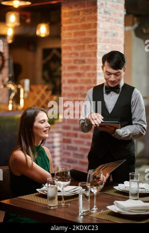 Lächelnde, elegante Frau, die im Restaurant Essen bestellte Stockfoto