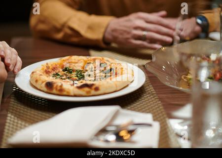 Kleine Pizza auf dem Teller vor der Frau, die im Restaurant zu Abend gegessen hat Stockfoto