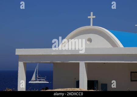 26. Mai 2022, Larnaca, Zypern: Das Segelboot fährt hinter der Agioi Anargyroi-Kirche am Kap Greco vorbei und liegt am Rand einer vertikalen Felsklippe über dem Meer. Es ist den Heiligen Kosmas und Damianos gewidmet. Unterhalb der Kapelle befindet sich eine Höhle mit dem heiligen Wasser der Heiligen. Die Republik Zypern steht an einem historischen und kulturellen Scheideweg zwischen Europa und Asien. Seine Hauptstädte - die Hauptstadt von Nikosia, Limassol, Famagusta und Paphos haben die Einflüsse von Generationen von Eroberern, Pilgern und Reisenden absorbiert und haben eine Atmosphäre, die sowohl kosmopolitisch als auch provinziell ist. (Bild: © Ruaridh Stockfoto