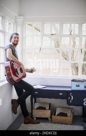 Die Lieder sind so süß, dass Sie sich mit einem Ständchen fühlen. Porträt eines hübschen jungen Mannes, der zu Hause Gitarre spielt. Stockfoto