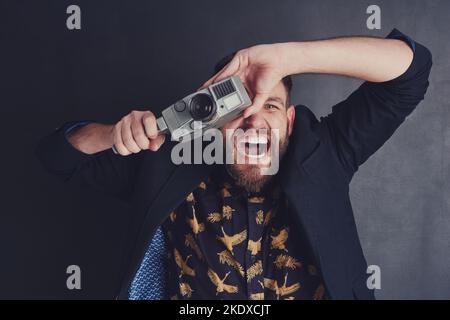 Er hat eine besondere Begeisterung für Filmkameras. Ein trendiger junger Mann mit einer Vintage-Kamera, die vor dunklem Hintergrund posiert. Stockfoto