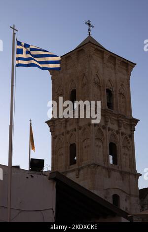 23. Mai 2022, Larnaka, Zypern: Die griechische Flagge fliegt neben dem Glockenturm der Lazarus-Kirche, die Ende des 9.. Jahrhunderts gegründet wurde und Architektur von byzantinischem, gotischem, barockem und Rokoko-Einfluss hat. Die Republik Zypern steht an einem historischen und kulturellen Scheideweg zwischen Europa und Asien. Seine Hauptstädte - die Hauptstadt von Nikosia, Limassol, Famagusta und Paphos haben die Einflüsse von Generationen von Eroberern, Pilgern und Reisenden absorbiert und haben eine Atmosphäre, die sowohl kosmopolitisch als auch provinziell ist. Heute ist Zypern ein beliebtes Touristenziel für Besucher aus Europa, bevorzugt b Stockfoto