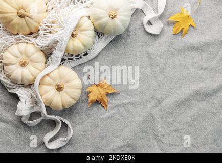 Draufsicht Herbstkomposition mit Kürbissen in Mesh-Einkaufstasche auf grauem Textilhintergrund Stockfoto