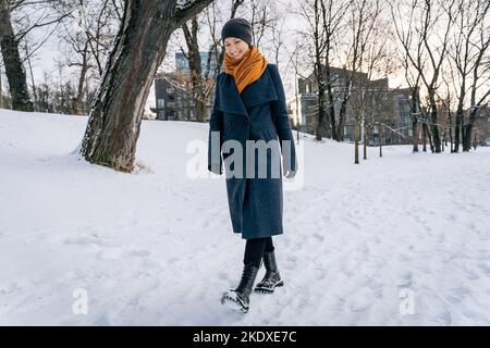 Eine Frau in Mantel, Schal, Hut und Stiefeln geht im Winter im Schnee. Stockfoto