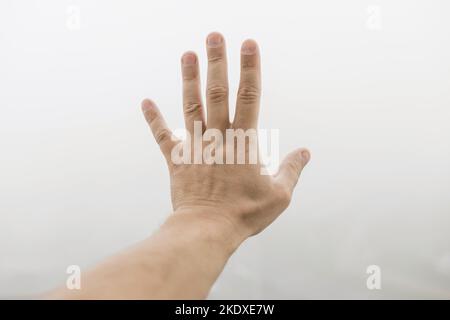 Die Hand eines Mannes zeigt fünf Finger im Nebel. Mystisches Konzept Stockfoto