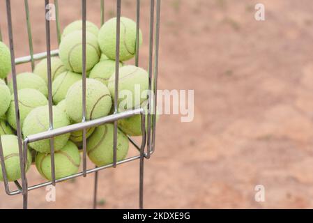 Tennisbälle im Korb auf dem Hintergrund des Tennisplatzes. Alte Tennisbälle. Platz kopieren Stockfoto