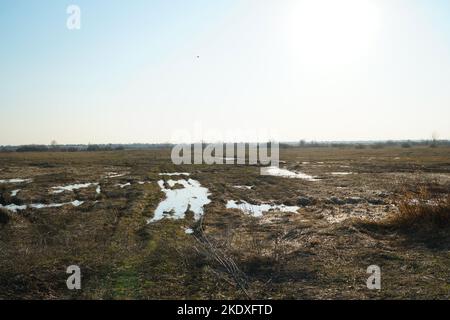 Pfützen auf einer unbefestigten Straße und einem wilden Feld während des Herbst- oder Frühjahrsauftauens. Im Herbst oder Frühling im Gelände Stockfoto