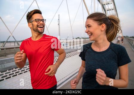 Workout am frühen Morgen. Glückliches Paar, das über die Brücke läuft. Ein gesunder Lebensstil. Stockfoto