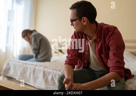 Verwirrt Mann schaut zu weinen Mädchen sitzt auf der gegenüberliegenden Seite des Bettes nach unangenehmen Gespräch Stockfoto