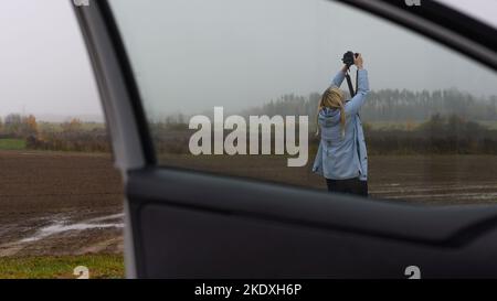 Suntaži, Lettland, 25. Oktober 2022: Professioneller Fotograf, der mit Nikon-Kamera auf dem Land fotografiert. Blick von einem Auto Stockfoto