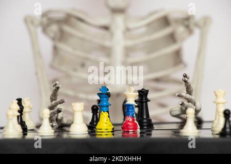 Schach mit einer gemalten Flagge Russlands und der Ukraine auf einem Schachbrett und einer Hand eines Skeletts auf dem Brett, dem Todesspiel der beiden Länder der Ukraine Stockfoto