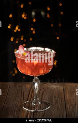 Schöner Cocktail mit Gin, Soda, Tonic Water, Erdbeere und Eis, garniert mit Rosenblume, auf Holzhintergrund. Cocktail für eine Party. Stockfoto