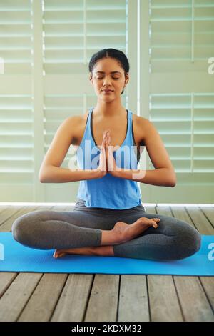 Wiederherstellung der Ruhe im Chaos des Alltags. Eine junge Frau meditiert, während sie zu Hause Yoga macht. Stockfoto