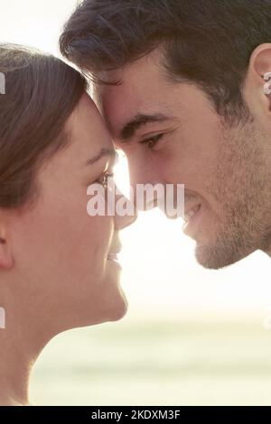 Sich in den Augen des anderen verirrt. Ein junges Paar genießt einen liebevollen Moment, während es sich draußen entspannt. Stockfoto