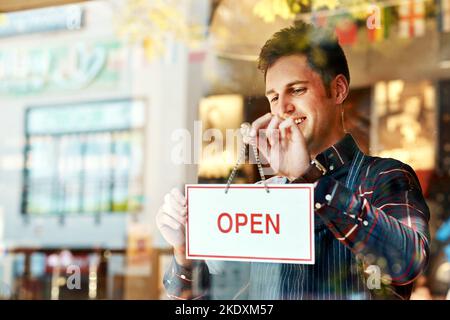 Die Eröffnung eines Restaurants erfordert Planung, Zeit, Geld und Leidenschaft. Nahaufnahme eines jungen Mannes, der ein offenes Schild an einem Schaufenster aufgehängt hat. Stockfoto