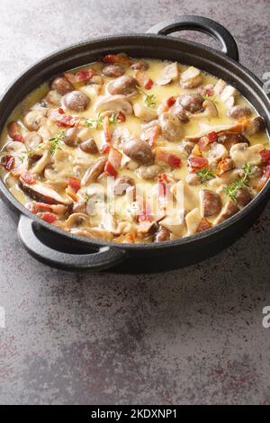 Champignon-Pilze in cremiger Weinsauce mit Speck und Parmesan in einer Pfanne auf dem Tisch. Vertikal Stockfoto