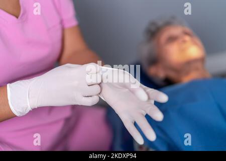 Von oben der Ernte unkenntlich weibliche Zahnarzt setzen auf Latexhandschuhe in der Nähe von älteren Patienten vor dem Eingriff in der modernen Zahnklinik Stockfoto