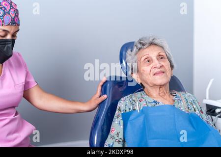 Ältere weibliche Patientin in legerer Kleidung mit Papierbätzchen sitzt auf einem bequemen Zahnstuhl während des Besuchs zum Crop Zahnarzt in der modernen Klinik Stockfoto