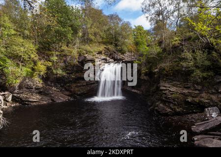 Atemberaubende Aussicht auf die Fallfälle von Fallloch, umgeben von üppigen Bäumen, an sonnigen Tagen in der Landschaft Schottlands Stockfoto