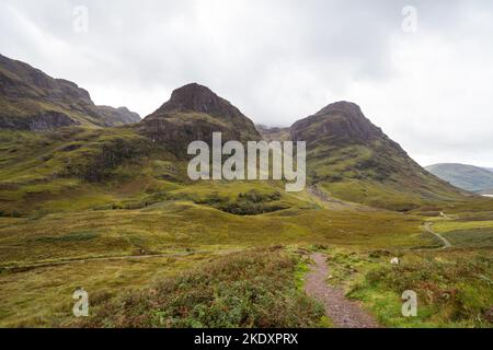 Atemberaubender Blick auf den Pfad, der in Richtung Bergkette führt, der sich gegen den bewölkten Himmel in Glen Coe, Schottland, befindet Stockfoto