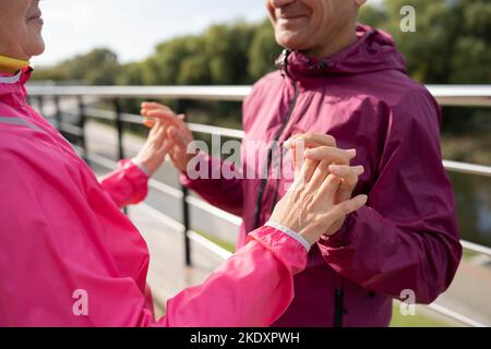 Crop reifen Sportler und Sportlerin in aktiven Ohr lächeln und die Hände zusammenklatschen, während in der Nähe von Zaun während Fitness-Training auf Damm Männer stehen Stockfoto