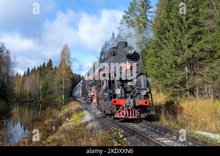 RUSKEALA, RUSSLAND - 09. OKTOBER 2022: Touristischer Retrozug des 'Ruskeala Express' am Ufer des Flusses Tokhmajokki an einem sonnigen Oktobertag Stockfoto