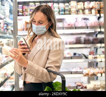 Lebensmittelgeschäft, Frau covid Maske und Telefon Lebensmittelzutaten Überprüfung eines Einzelhandelskunden. Lebensmittelgeschäft einer Person, die eine mobile App für eine gesunde Stockfoto