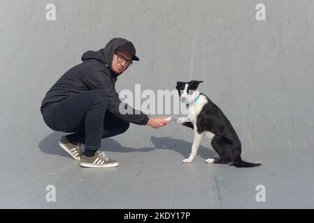 Ein Mann schüttelt die Pfote eines Hundes und posiert Stockfoto
