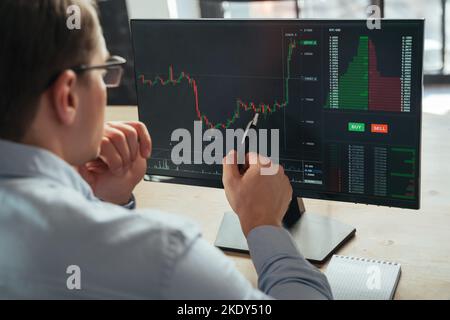 Nahaufnahme eines Finanzanalysten und Händlers, der aufmerksam Investmentgraph untersucht und versucht, zukünftige Aktionen des Geldflusses mit der Kryptowährungs-App vorherzusagen, wobei er mit dem Stift auf den Bildschirm zeigt Stockfoto