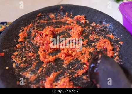 Gemahlener roter Chili mit traditionellen indonesischen Werkzeugen namens Cobek aus Stein. Stockfoto