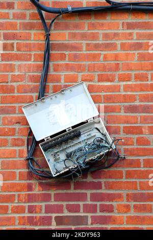 Eine Telefonbox für den Außenbereich mit verwickelten Drähten und Korrosion, die zufällig an einer Ziegelwand hängt. Stockfoto