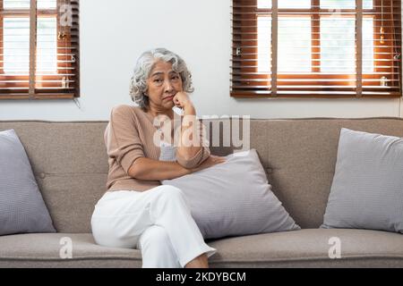 Asiatische ältere Frau im Wohnzimmer des Pflegeheims fühlt sich traurig, wenn sie unglücklich fehlt, nachdenklich in der psychischen Gesundheitsversorgung bei älteren Menschen. Stockfoto