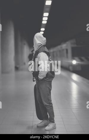 Eine Graustufenaufnahme eines jungen Mannes mit Hoodie und Skateboard in der U-Bahnstation, Porto, Portugal Stockfoto