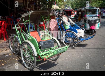 Zwei traditionelle Cyclos (Pedicabs) parkten auf einem Bürgersteig neben Tuktuks im Zentrum von Phnom Penh, Kambodscha. Stockfoto