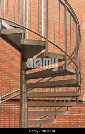 Eine vertikale Aufnahme einer verdrehten Metalltreppe in der Nähe einer orangefarbenen Ziegelwand Stockfoto