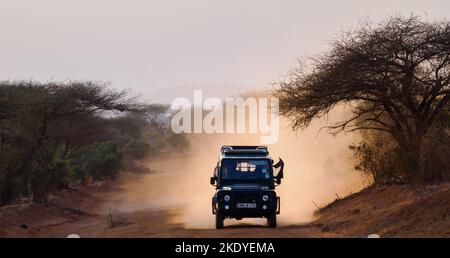 Land Rover Safari-Fahrzeug, das bei einer abendlichen Fahrt im Tsavo National Park in Kenia, Ostafrika, Staub aufwirbelt Stockfoto
