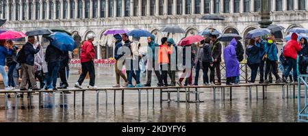 Touristen in einer regnerischen Venedig mit duckboards über eine überschwemmte St Mark's Platz bei Flut zu gehen Stockfoto