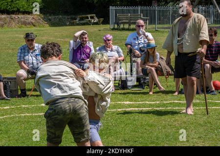 Ein Schiedsrichter stickler beobachtet zwei junge Jungen, die beim Grand Cornish Wrestling Tournament auf dem malerischen Dorfgrün von St. Mawgan teilnehmen Stockfoto