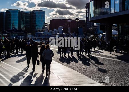 Menschenmassen neben dem Tower of london am Tower Millennium Pier. Lange Schatten von Figuren, die der Sonne mit starker Hintergrundbeleuchtung gegenüberstehen Stockfoto